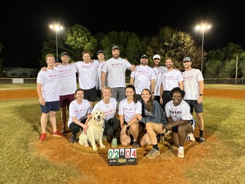 residents softball team with a dog posed at a pitcher's mound at night